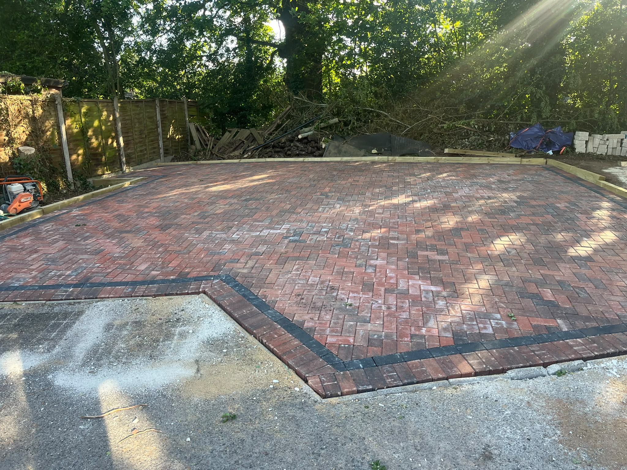 Red herringbone block patio with a black brick border in a garden